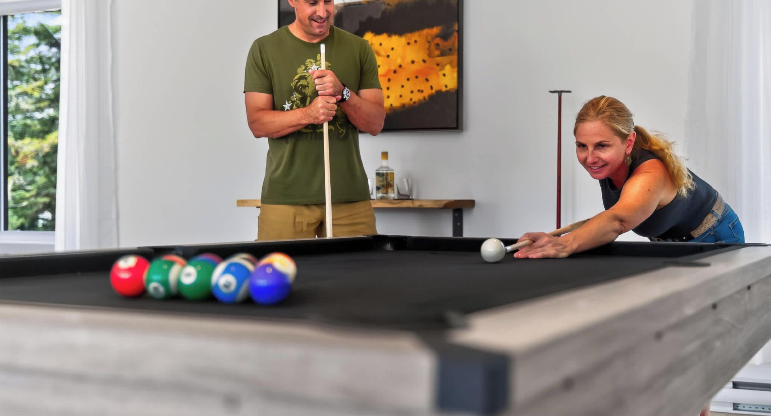 A pool table with balls, a person leaning over it, and another person standing behind.