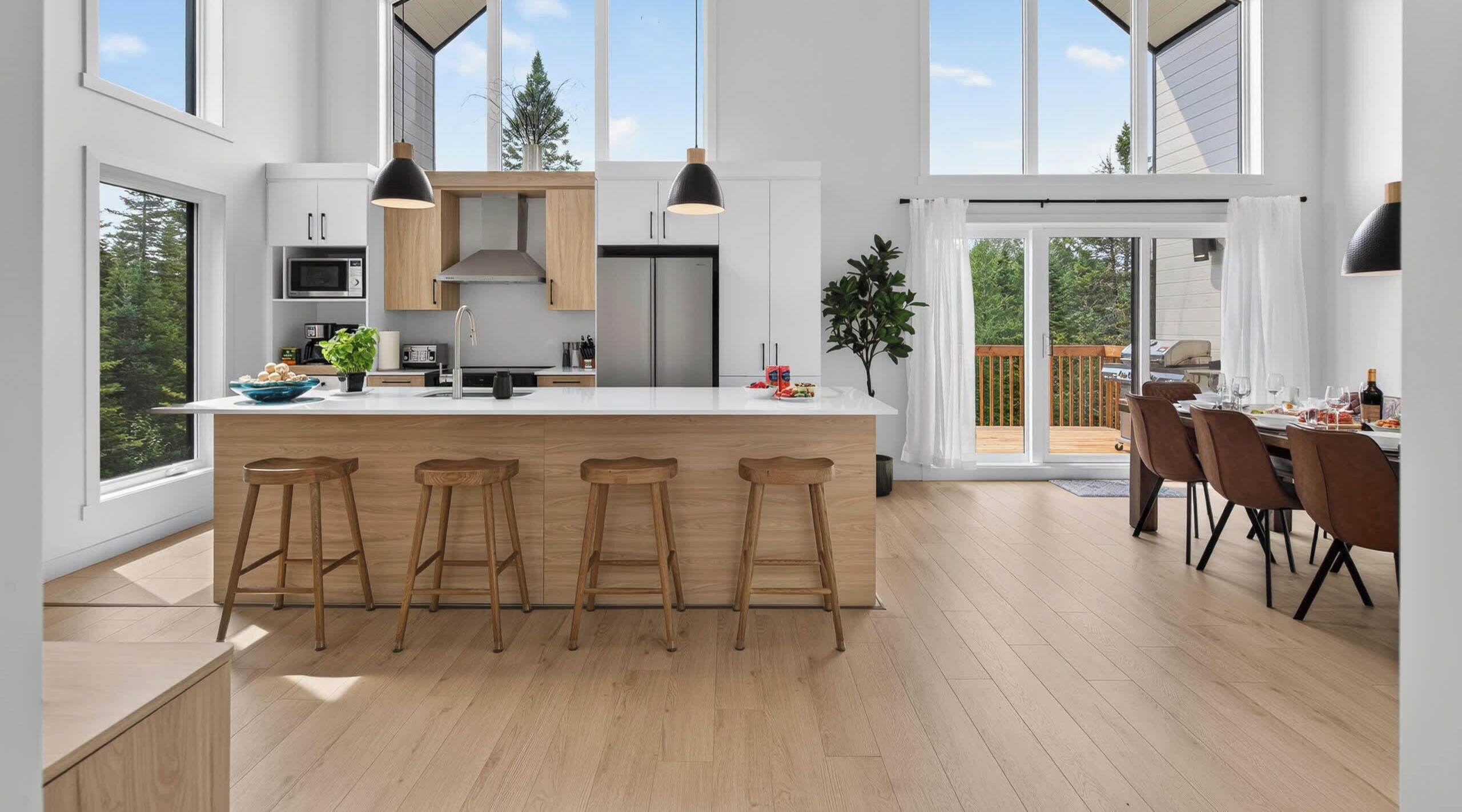 A modern kitchen with a central island, bar stools, and a dining area with a view of the outdoors.
