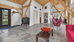 A spacious room with a high ceiling and exposed wooden beams, a red bowl on a table, a hammock, and a red sofa.
