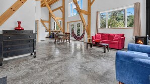 A spacious living area with a high ceiling, a fireplace, a red sofa, a blue armchair, and a dining area with a table and chairs.