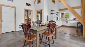 A spacious kitchen with wooden beams, a dining area with a table and chairs, and a view of the outdoors through a window.