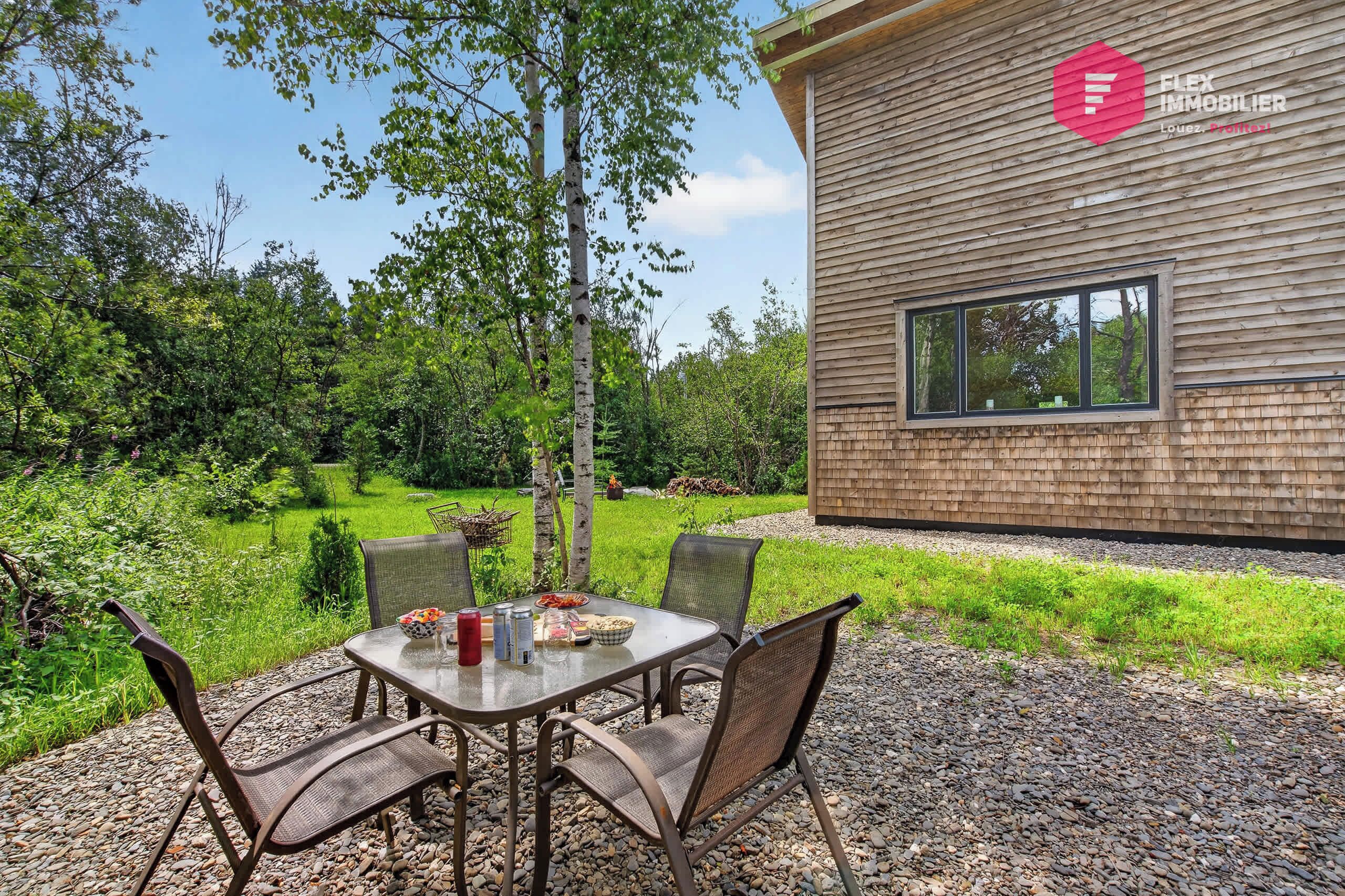 A modern outdoor dining area with a table and chairs, surrounded by a gravel path and greenery.