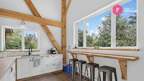 A modern kitchen with wooden beams, white cabinets, a large window, and a bar area with stools.