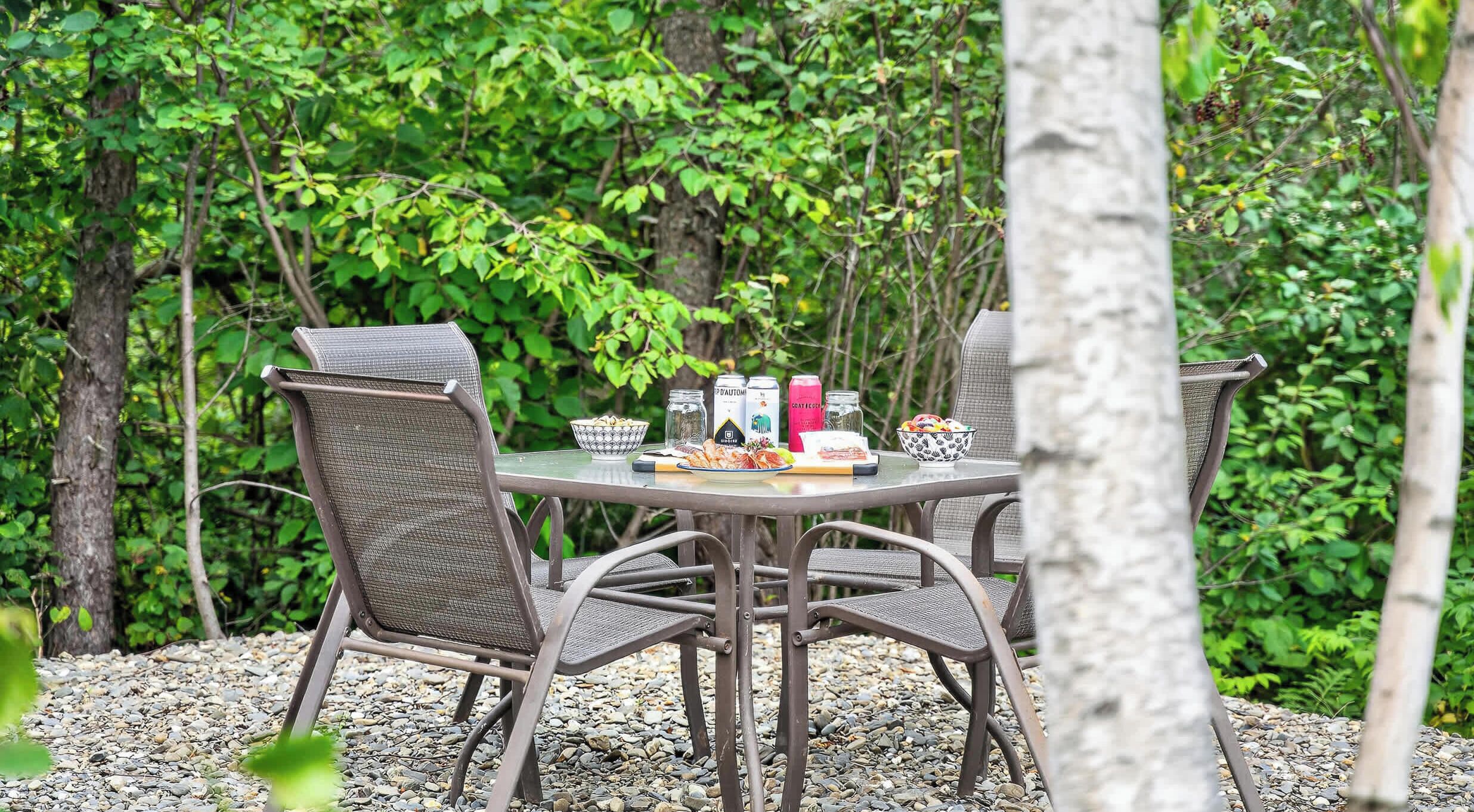 Un área de comedor al aire libre con mesa y sillas, rodeada de follaje.