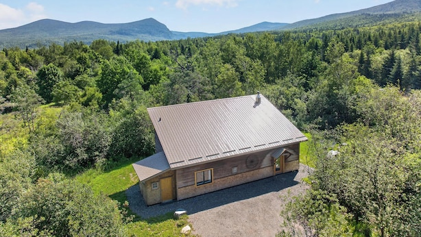 A cabin with a sloped roof, surrounded by dense forest and mountains in the background.