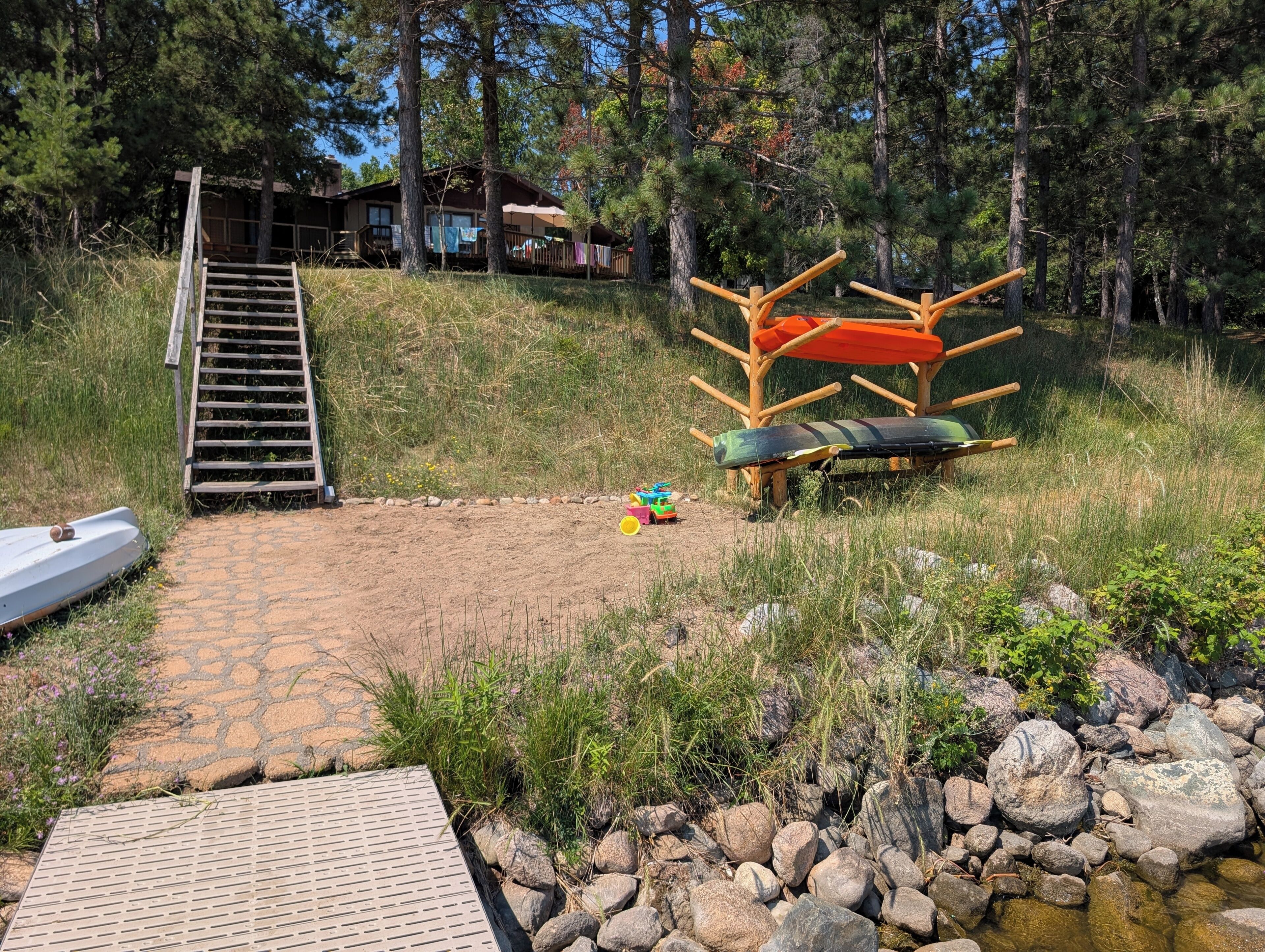 A wooden deck, a ladder, a small boat, a children's play area, and a wooden structure with a roof.