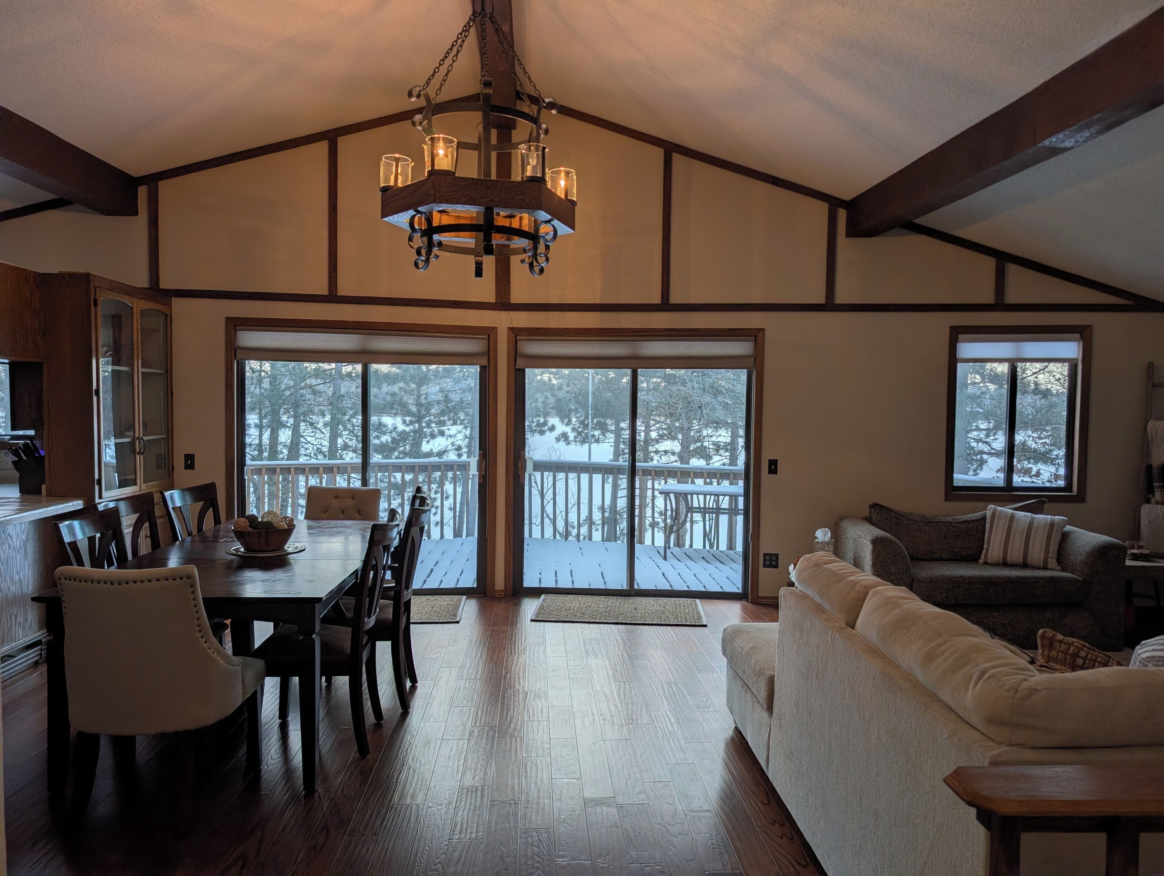 A spacious living area with a dining table, chairs, a sofa, and a large sliding glass door leading to a deck.