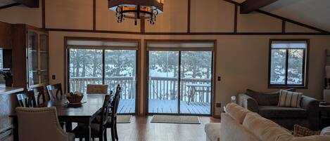 A spacious living area with a dining table, chairs, a sofa, and a large sliding glass door leading to a deck.