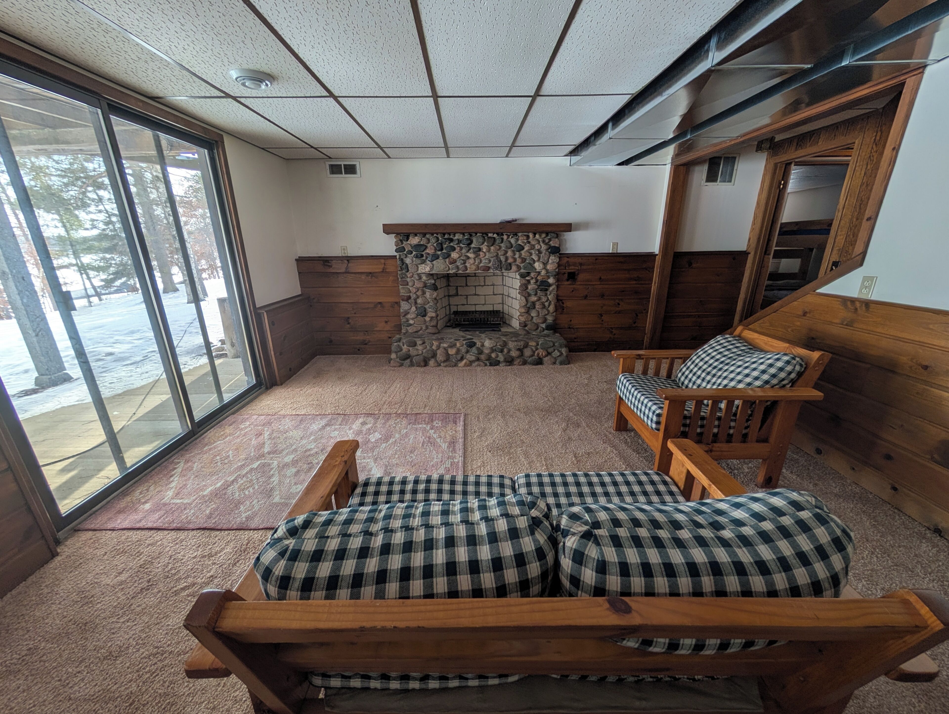 A room with a stone fireplace, wooden furniture, and a large window.