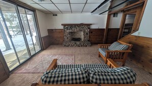 A room with a stone fireplace, wooden furniture, and a large window. - 4-bedroom family lake house near Park Rapids with air conditioning (Nevis)