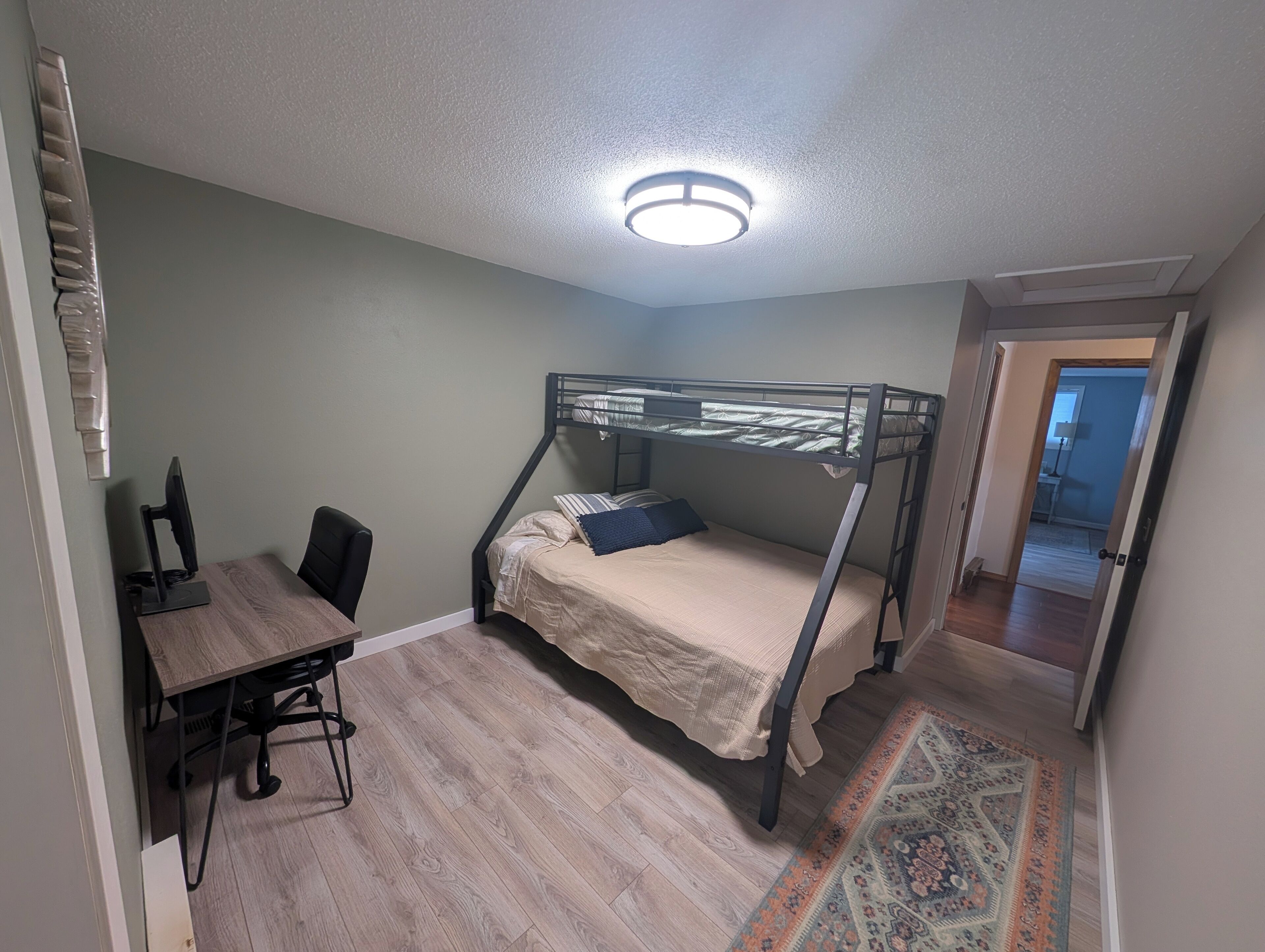 A room with a bunk bed, a desk with a chair, a computer, and a patterned rug.