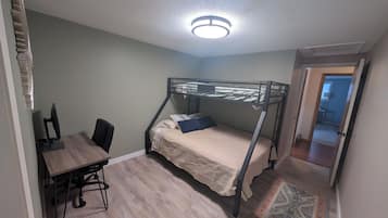 A room with a bunk bed, a desk with a chair, a computer, and a patterned rug.