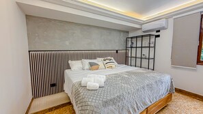 A bedroom with a bed, a headboard, a shelf with decorative items, and an air conditioning unit. - Primavera Lofts (Medellín)