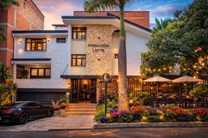 Un hôtel moderne avec une façade en pierre, des places assises à l’extérieur et une voiture garée devant.