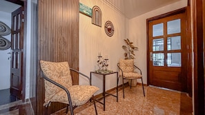 Un couloir avec deux chaises, une petite table ornée de bougies et une porte en bois dotée de panneaux de verre.