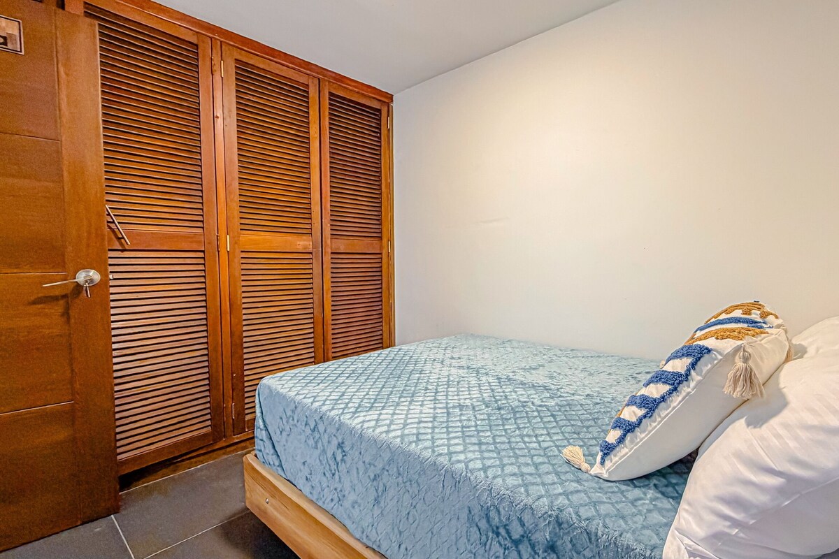 Une chambre à coucher avec un lit, des oreillers blancs, une couverture bleue et une armoire en bois.