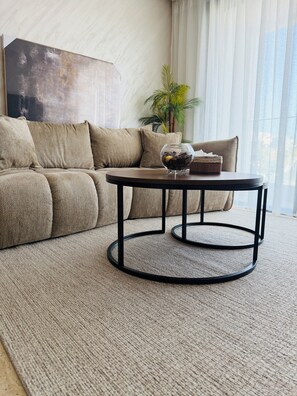 A living room with a beige sofa, a round coffee table with a glass top, and a potted plant. - Cozy 2-Bedroom Apartment in Center of Tangier - AC & Terrace (Tangier)