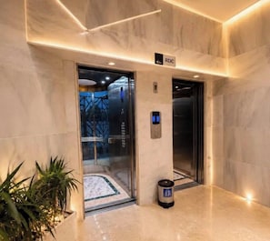 An elevator with a digital display, a trash bin, and a sign labeled 'RDC' in a modern lobby with marble flooring and a plant. - Cozy 2-Bedroom Apartment in Center of Tangier - AC & Terrace (Tangier)
