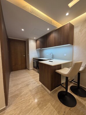 Una cocina moderna con una isla central, armarios de madera oscura, horno empotrado y un lavamanos. Hay dos taburetes de bar y una lámpara sobre la isla.