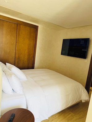 A hotel room with a bed, a TV mounted on the wall, and a wooden headboard. - Cozy 2-Bedroom Apartment in Center of Tangier - AC & Terrace (Tangier)