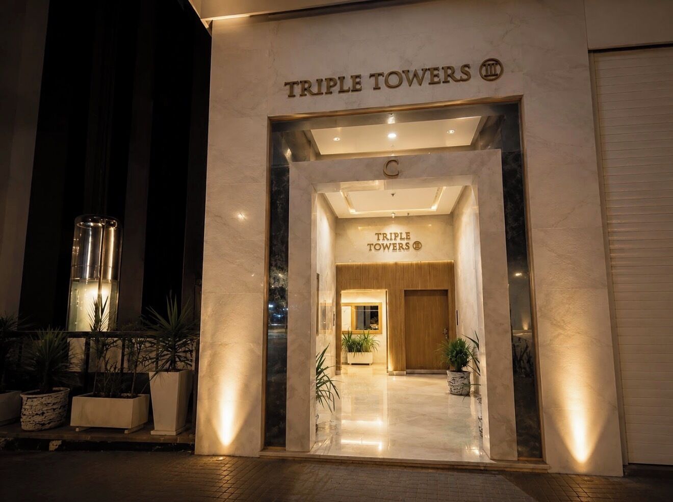 The entrance to Triple Towers hotel with a modern facade and a welcoming interior.