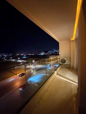 Un balcón con vista a un paisaje urbano nocturno, que incluye una calle con vehículos en movimiento y luces de la ciudad a lo lejos.