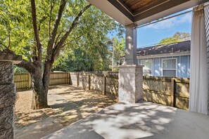 A covered patio area with a stone wall, a wooden fence, and a tree providing shade. - Fully Furnished 3BR East Nashville Home | 30+ Days (Nashville)