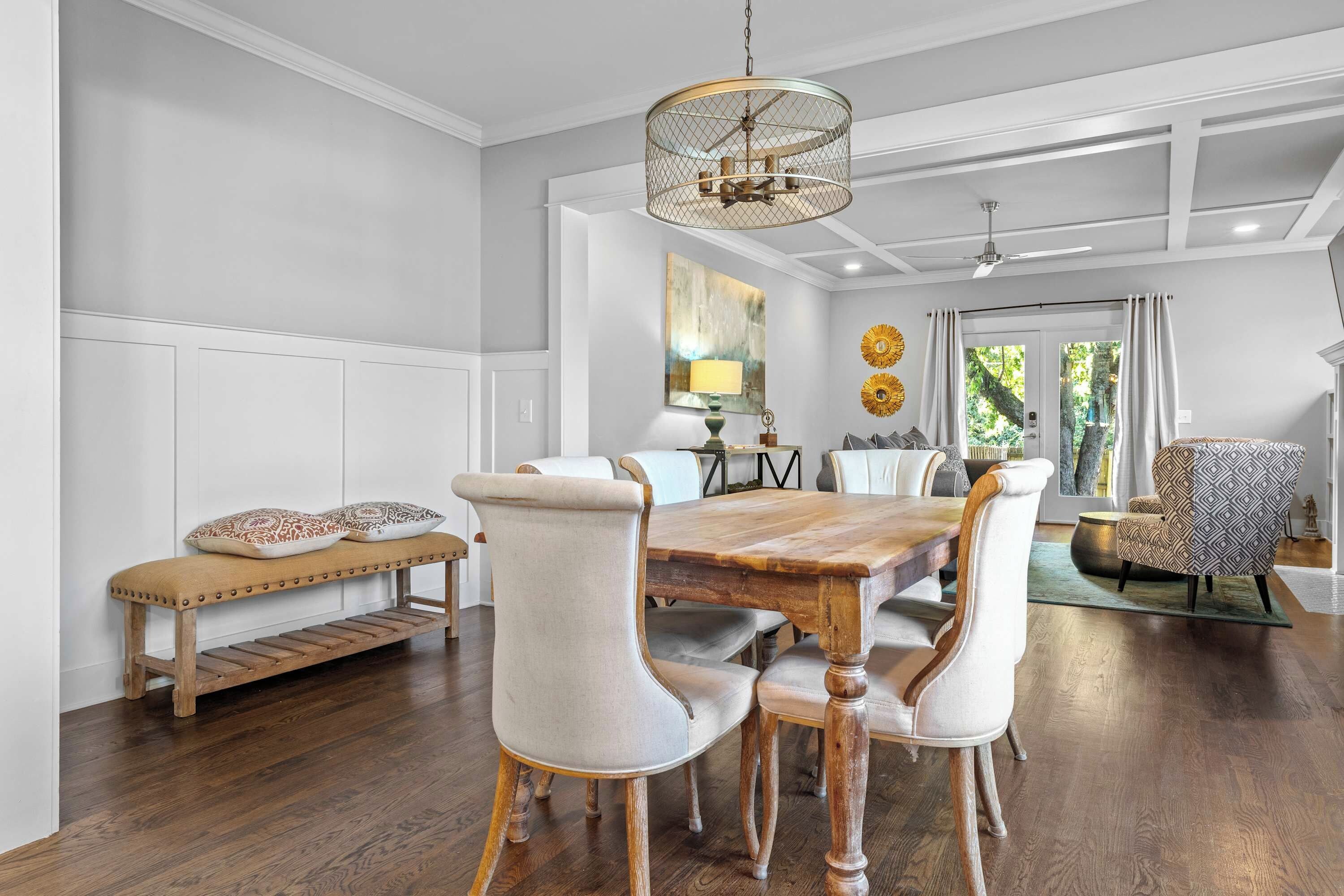 A dining area with a wooden table, upholstered chairs, a bench, and a decorative ceiling light.