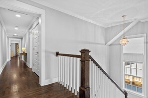 A hallway with a wooden staircase, white railings, and a hanging light fixture. - Fully Furnished 3BR East Nashville Home | 30+ Days (Nashville)