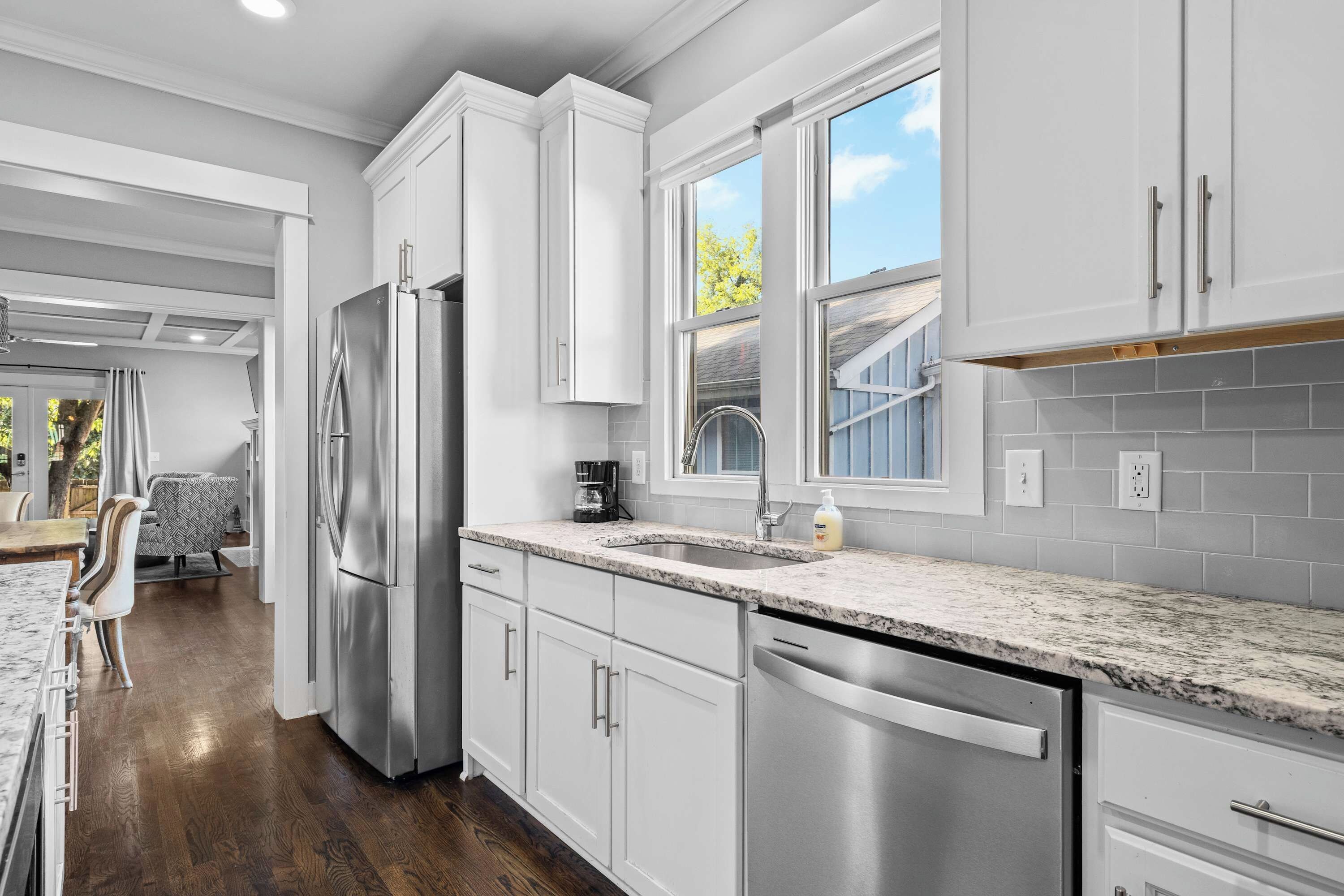 A modern kitchen with stainless steel appliances, white cabinetry, and a large window providing natural light.