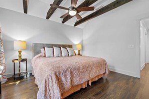 Ein Schlafzimmer mit einem Bett, zwei Nachttischlampen, einem Deckenventilator und Holzbalken.
