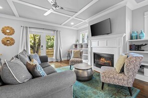 A modern living room with a fireplace, a ceiling fan, and a television mounted on the wall. - Fully Furnished 3BR East Nashville Home | 30+ Days (Nashville)