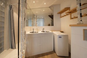 A modern bathroom with a glass shower enclosure, a double sink vanity, and a white washing machine. - Majestic Panorama - Stunning Mont Blanc Views|Fireplace|Central Chamonix (Chamonix-Mont-Blanc)