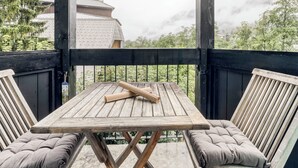 Um deck de madeira com uma mesa e duas cadeiras acolchoadas, com vista para uma paisagem montanhosa.
