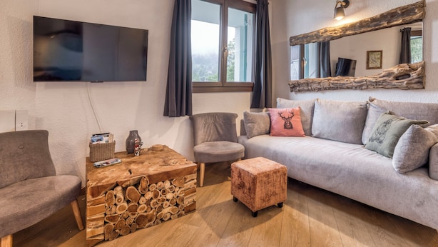 Sala de estar com televisão de tela plana, sofá, mesa de centro com design de tronco e janela com cortinas.
