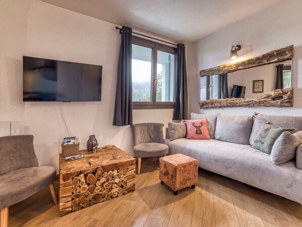 A living room with a flat-screen TV, a sofa, a coffee table with a log design, and a window with curtains. - Marmottons - Comfortable 2-bedroom apartment (Chamonix-Mont-Blanc)
