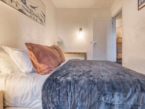 A bedroom with a bed, pillows, a wall-mounted light, and a door leading to another room. - Marmottons - Comfortable 2-bedroom apartment (Chamonix-Mont-Blanc)