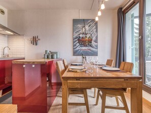 Une cuisine moderne avec une table à manger en bois pour quatre personnes, un meuble rouge et un tableau représentant une bouteille de vin accroché au mur.