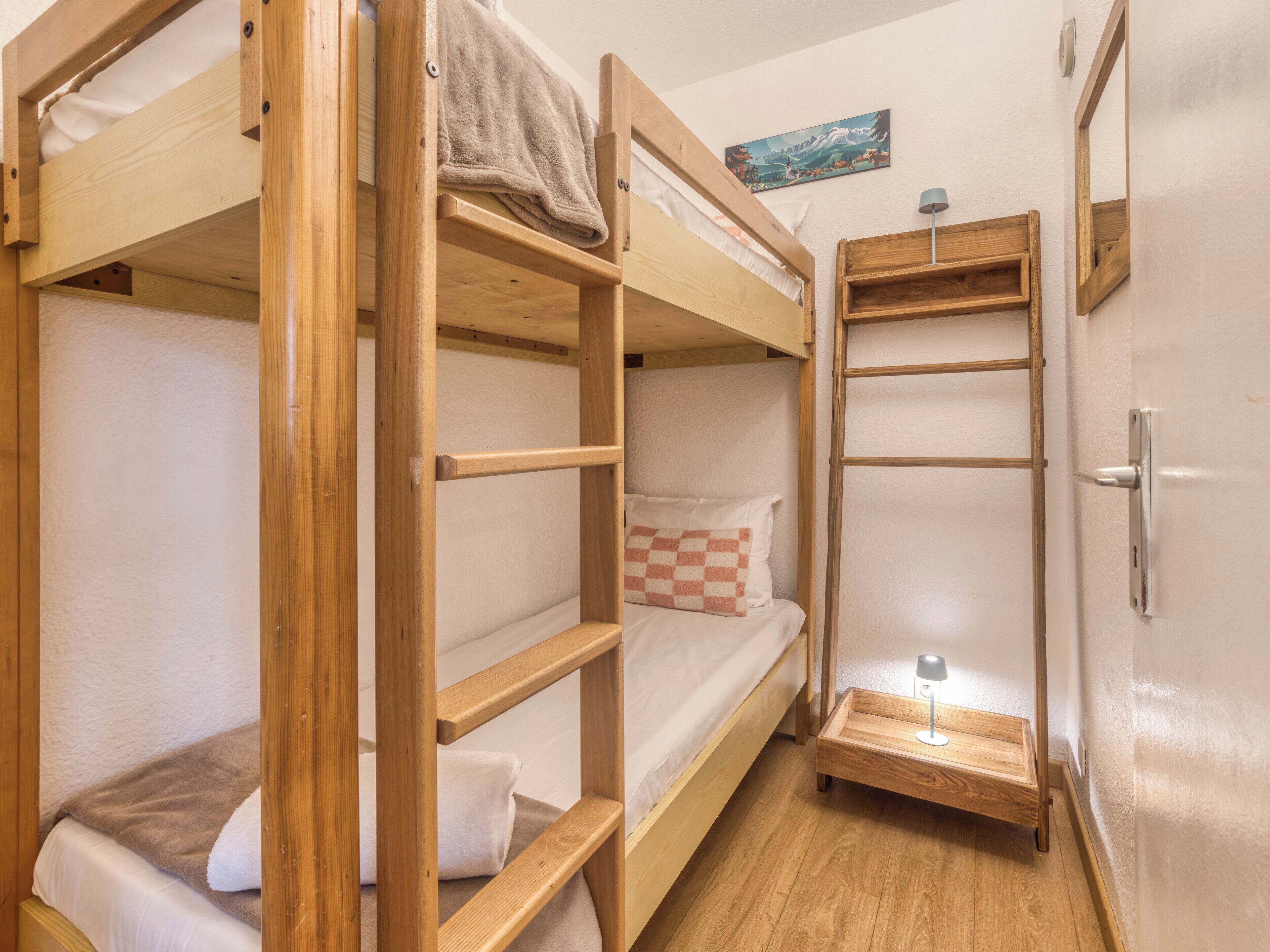 Une chambre avec un lit superposé, une échelle en bois, une petite table de chevet avec une lampe et un tableau accroché au mur.