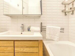 A bathroom with a white sink, wooden cabinet, and a bathtub. - Marmottons - Comfortable 2-bedroom apartment (Chamonix-Mont-Blanc)