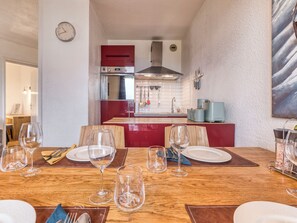 A dining area with a wooden table set for four, a kitchen in the background, and a clock on the wall. - Marmottons - Comfortable 2-bedroom apartment (Chamonix-Mont-Blanc)