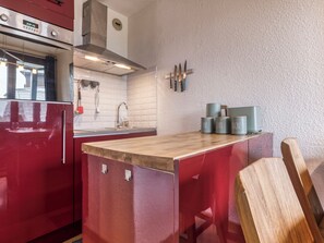 Une cuisine avec un réfrigérateur rouge, un four en acier inoxydable, un îlot central en bois et un porte-couteaux fixé au mur.
