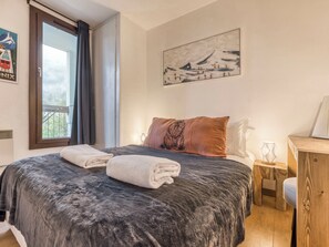 A bedroom with a bed, a window, a painting, and a wooden nightstand. - Marmottons - Comfortable 2-bedroom apartment (Chamonix-Mont-Blanc)