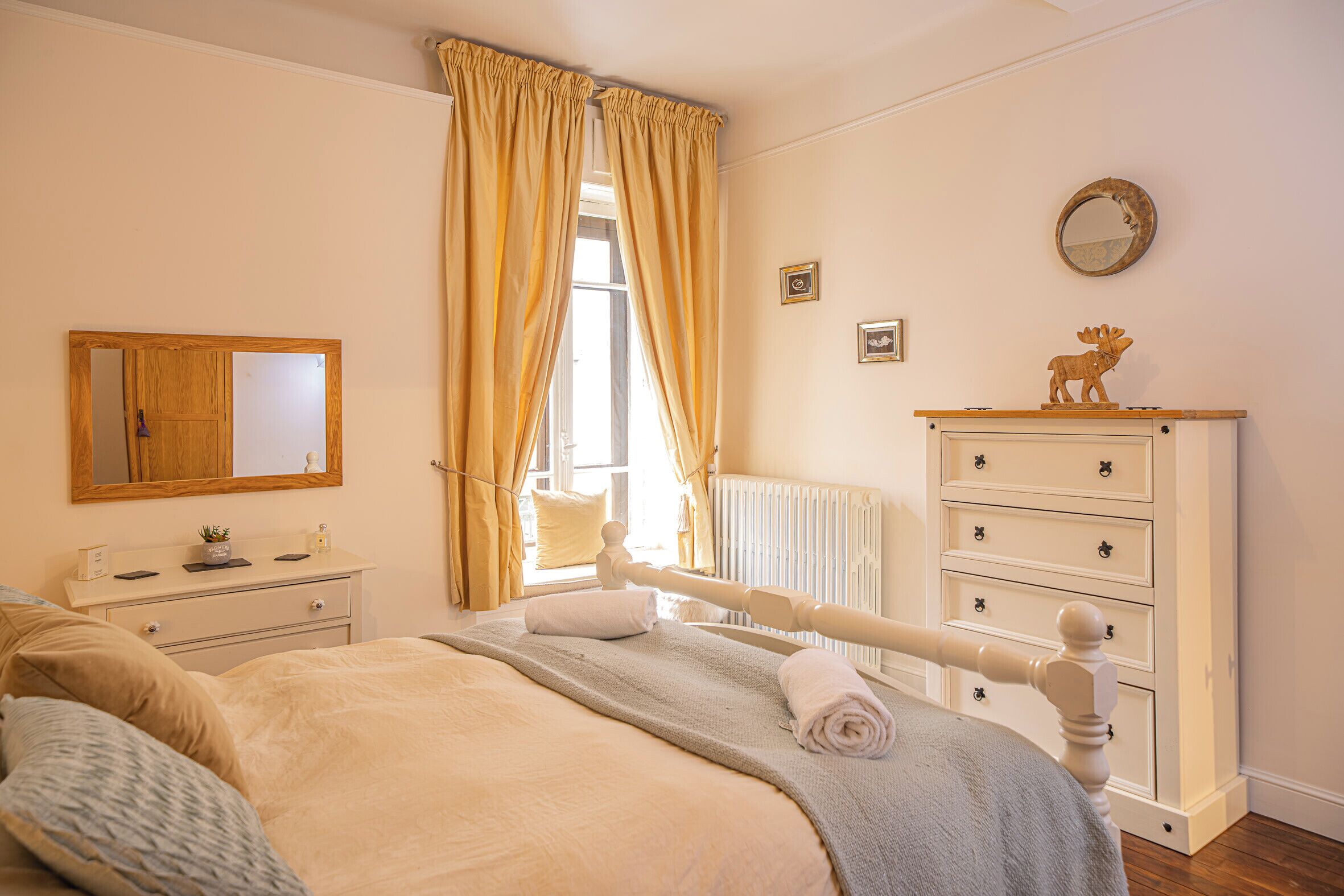 A bedroom with a bed, a dresser, a mirror, a radiator, and a window with curtains.