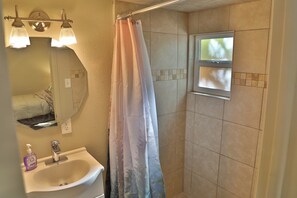 Ein Badezimmer mit Dusche, Waschbecken, Spiegel und Fenster.