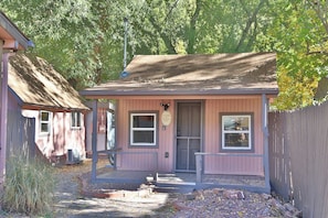 A small pink cabin with a porch, a door, and a window. - NEW! On The Creek. Cozy. 1 BR 1 BA Cabin. Downtown Manitou Springs. New Hot Tub! (Manitou Springs)