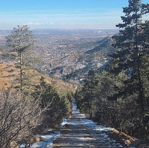 A pathway leading through a forested area with a view of a distant town. - NEW! On The Creek. Cozy. 1 BR 1 BA Cabin. Downtown Manitou Springs. New Hot Tub! (Manitou Springs)