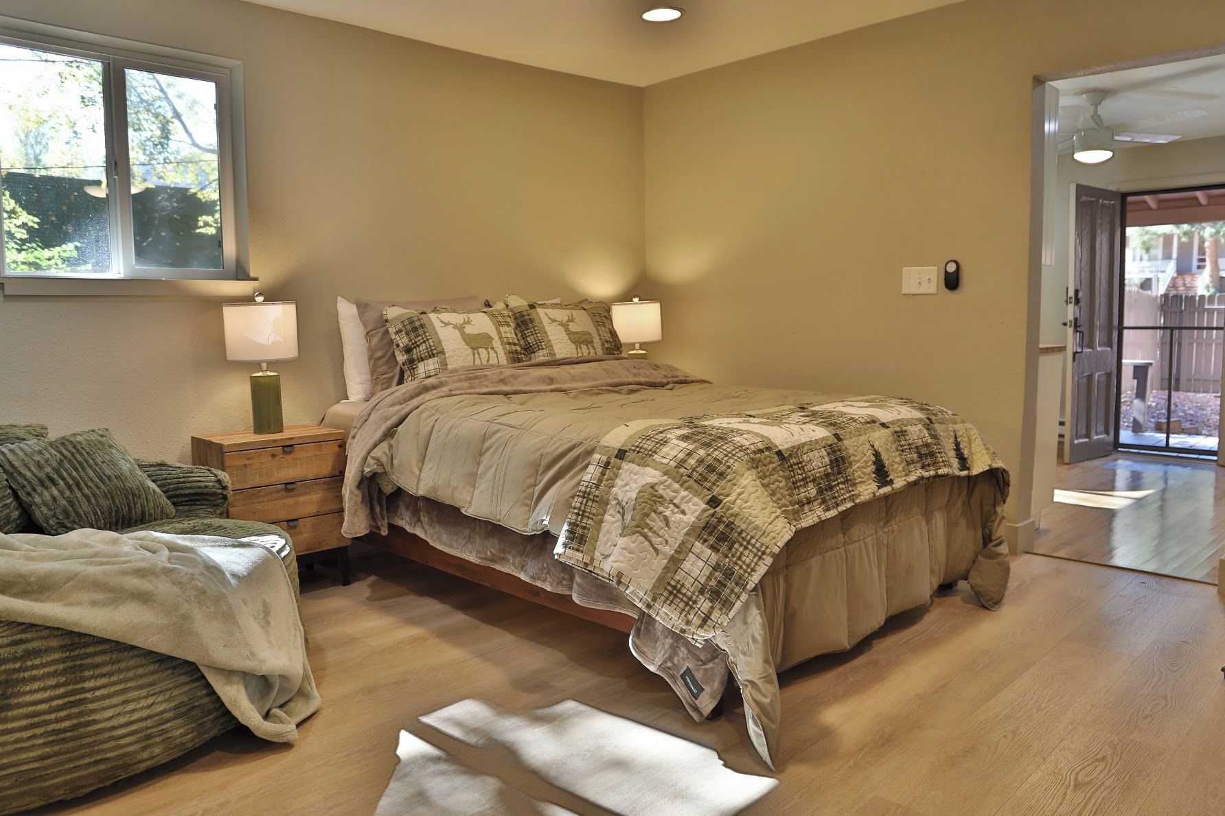 Une chambre à coucher avec un lit, des lampes de chevet, une table de chevet en bois, une fenêtre et une porte donnant sur l’extérieur.