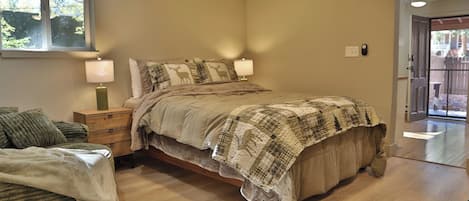 Un dormitorio con cama, lámparas de noche, una mesita de noche de madera, una ventana y una puerta que da al exterior.