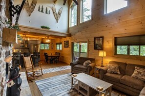 Ein gemütliches Blockhaus-Interieur mit Essbereich, Wohnzimmer mit Sofa und Tisch sowie einer durchgehenden Tür erkennbaren Küche.